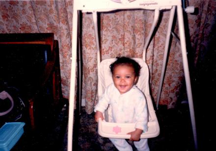 Sharee smiling as a toddler in a bouncy swing.